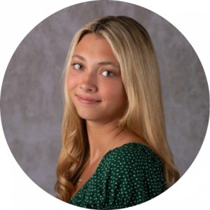 A headshot of Katie Myjak. She is looking over her shoulder at the camera and is smiling with her mouth closed.